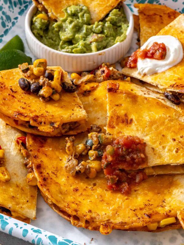 Sheet pan quesadilla wedge dipped into guacamole with crispy quesadilla wedges, salsa, Greek yogurt and lime
