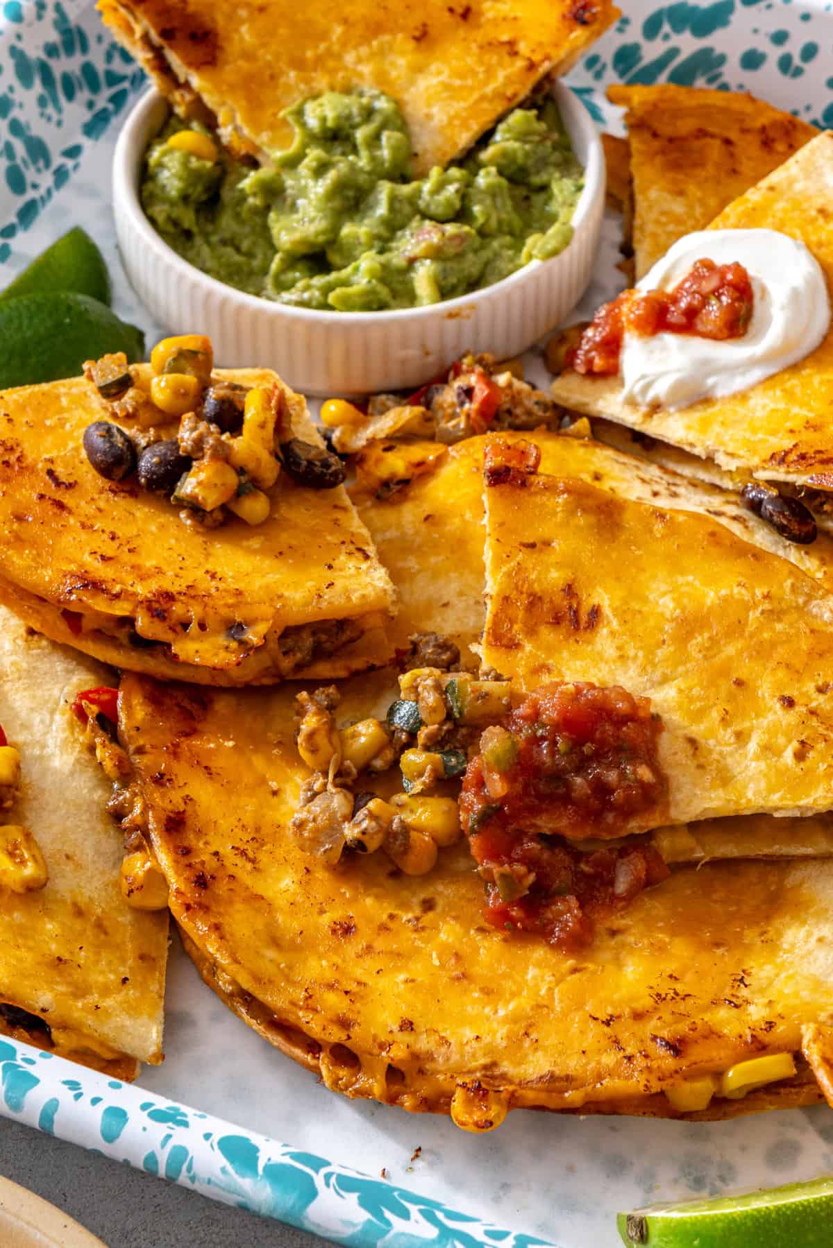 Sheet pan quesadilla wedge dipped into guacamole with crispy quesadilla wedges, salsa, Greek yogurt and lime