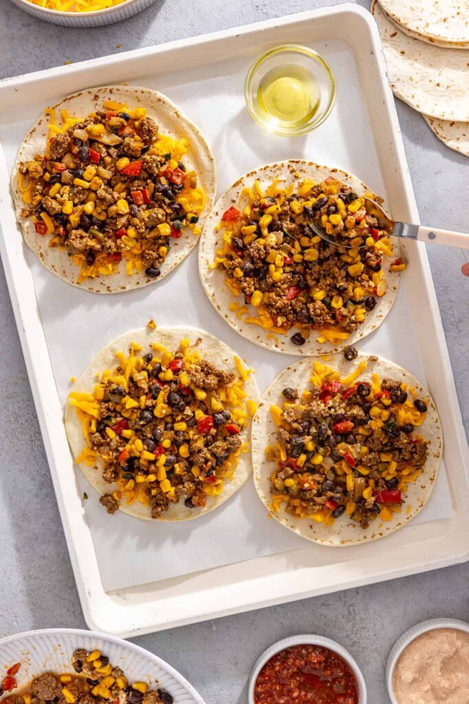 Leftover street corn taco filling spread over tortillas for sheet pan quesadillas