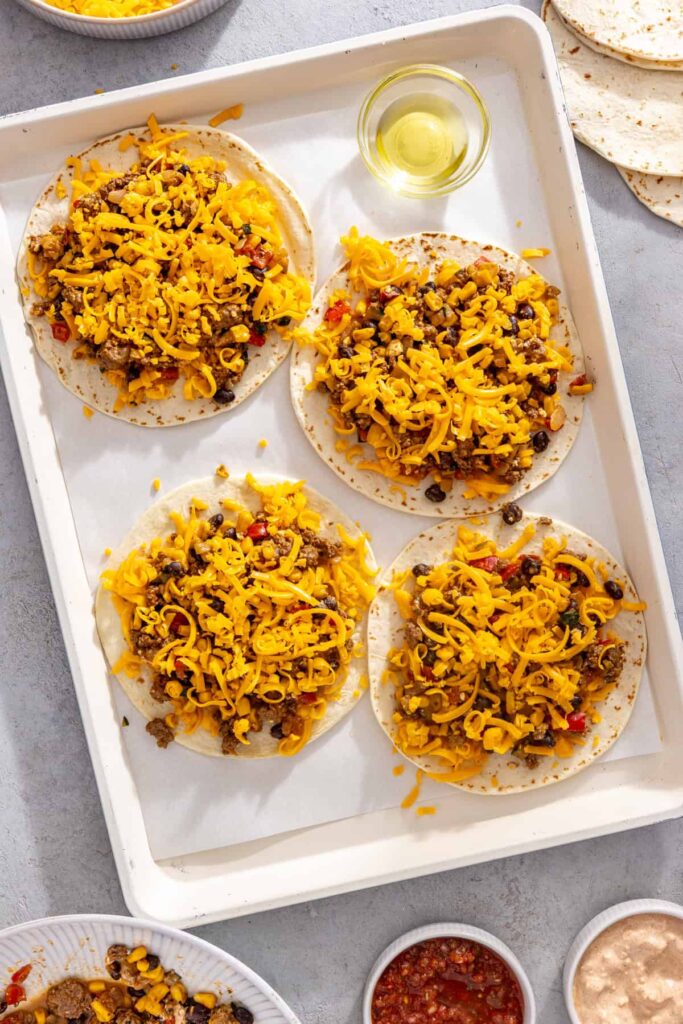 Shredded cheddar cheese sprinkled over street corn taco filling for sheet pan quesadillas