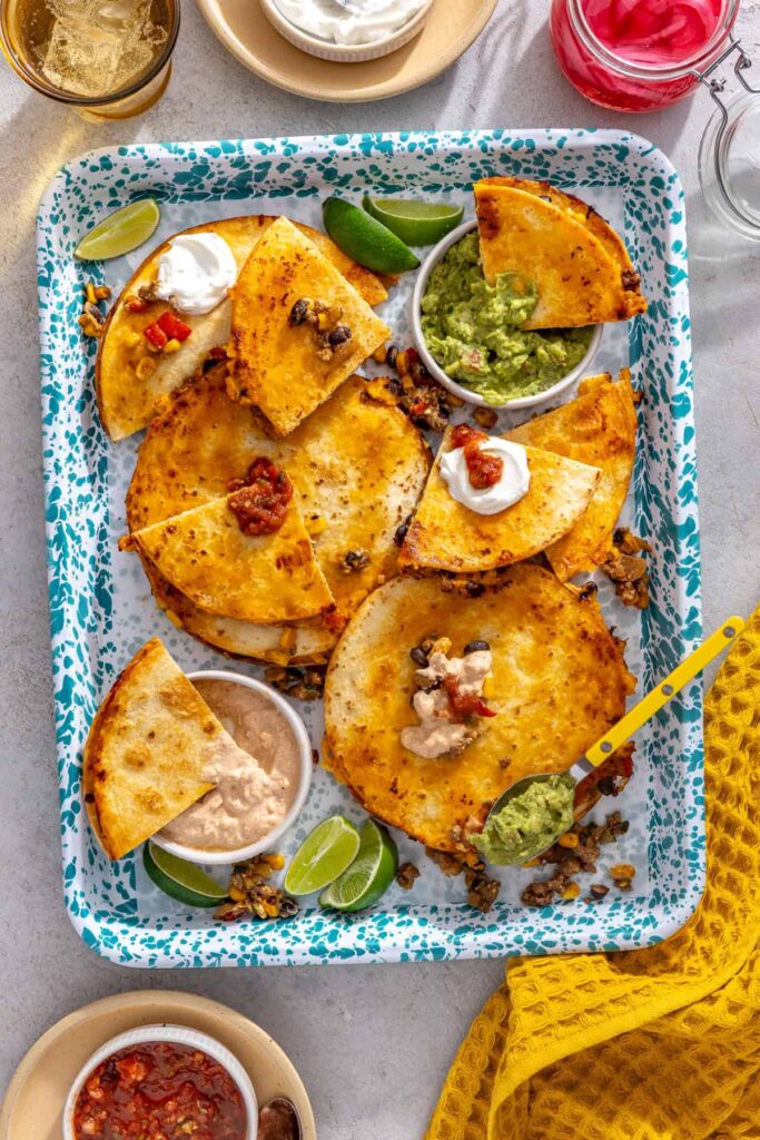 Easy sheet pan quesadillas served on a splatter tray with lime wedges and dipping sauces