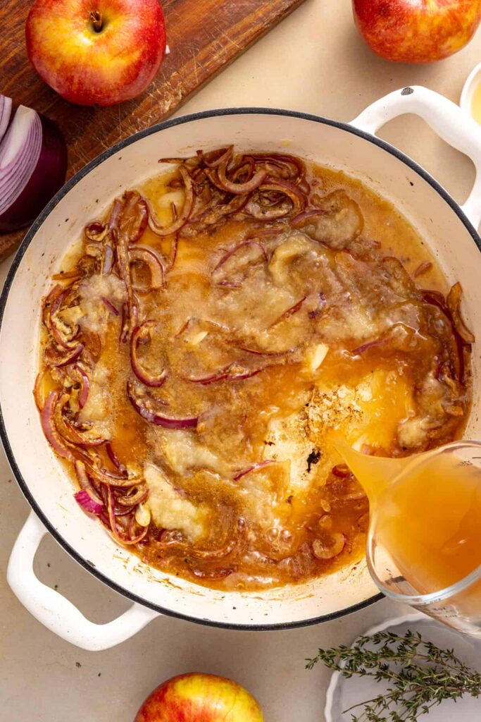 pouring apple cider vinegar base into a skillet with sauteed red onion, garlic, and dijon mustard for slow cooker pork