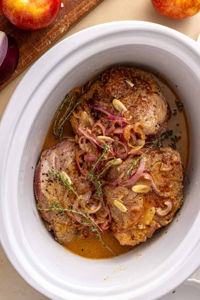 Seared pork shoulder nestled in apple cider sauce with fresh thyme before slow cooking.