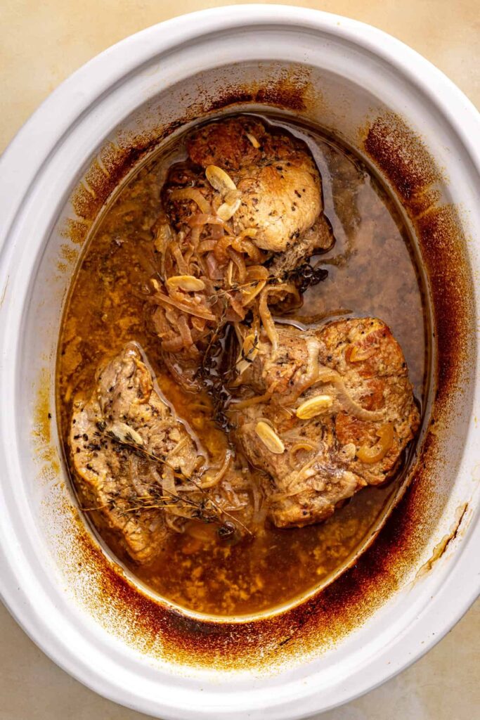Slow-cooked pork shoulder in a savory apple cider sauce before adding apples and onion wedges.