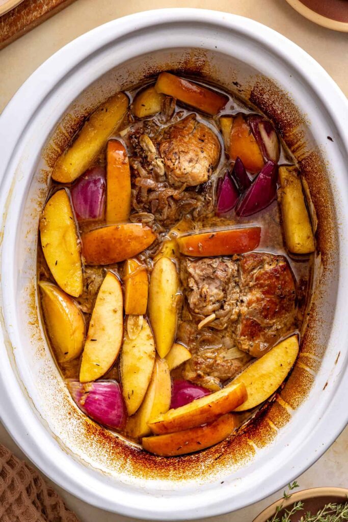 Slow cooker pork surrounded by fresh apple wedges, red onion, and thyme in cider gravy.