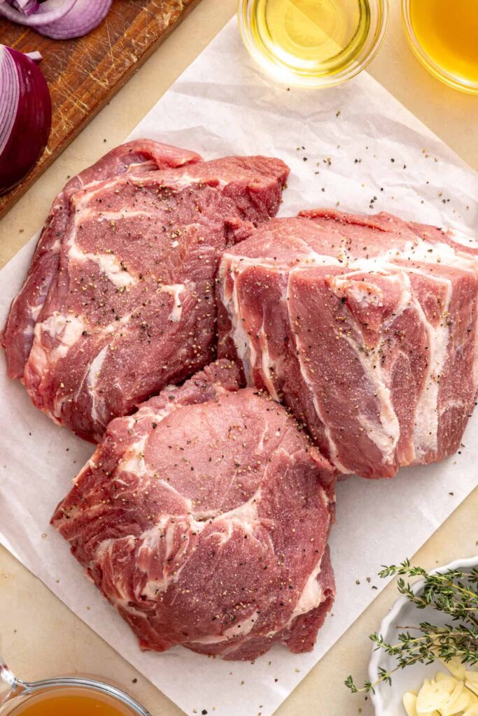 Boneless pork shoulder pieces seasoned with salt and freshly ground black pepper before searing.