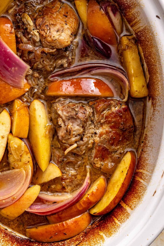 close up of tender slow-cooked pork shoulder with softened apple and red onion wedges