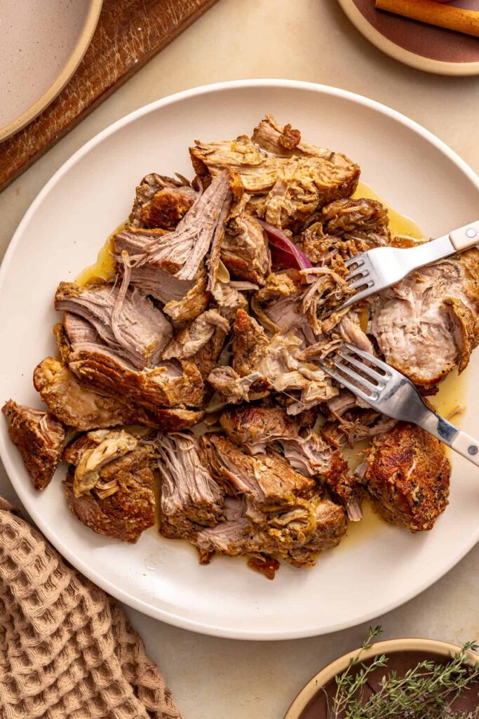 Tender slow-cooked pork shoulder being shredded with two forks into bite-sized pieces.