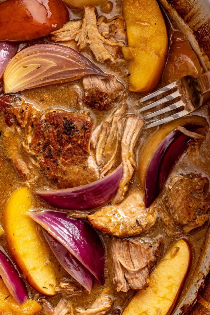 Shredded pork shoulder and apple wedges in cider gravy, with a fork resting beside the tender meat.