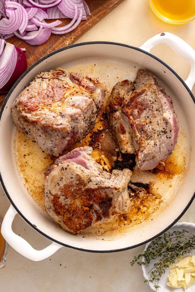 Boneless pork shoulder developing a golden-brown crust in a skillet before slow cooking.