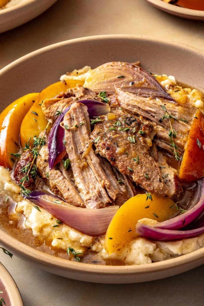 Close side-angle view of apple cider braised pork over mashed potatoes, garnished with fresh thyme.