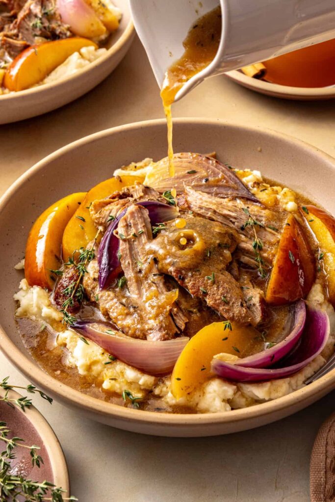 Apple cider gravy being poured over shredded pork and mashed potatoes from a gravy boat.