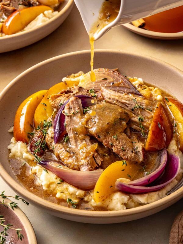 Slow cooker apple cider pork served over mashed potatoes with fresh thyme as cider gravy is poured over the top.