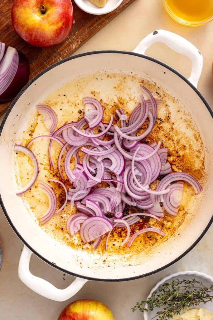 Thinly sliced red onion softening in the skillet with browned bits from the seared pork.