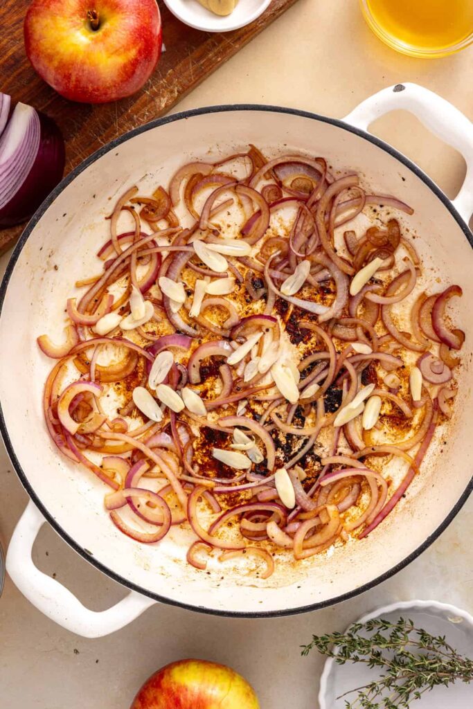 Thinly sliced garlic cooking with softened red onion in a skillet until fragrant.