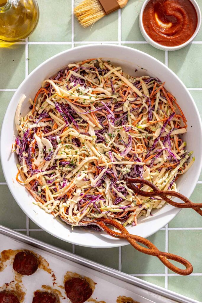 Tossing shredded cabbage, carrots, and green apple until evenly coated in creamy Greek yogurt ranch.