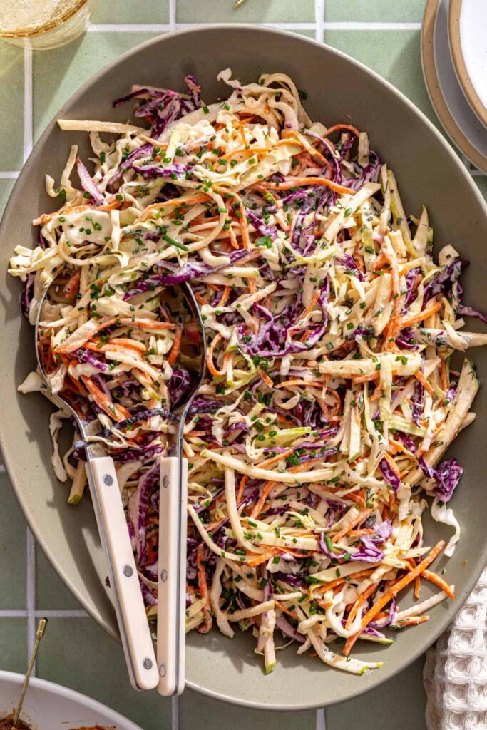 Crunchy green and red cabbage slaw tossed in creamy herb ranch dressing in a serving dish.