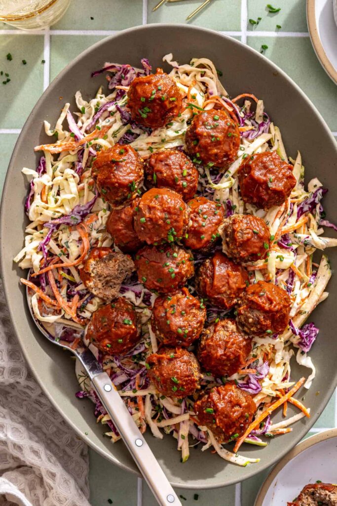 Serving platter of sticky BBQ meatballs over homemade ranch slaw, ready for an easy family dinner or appetizer.