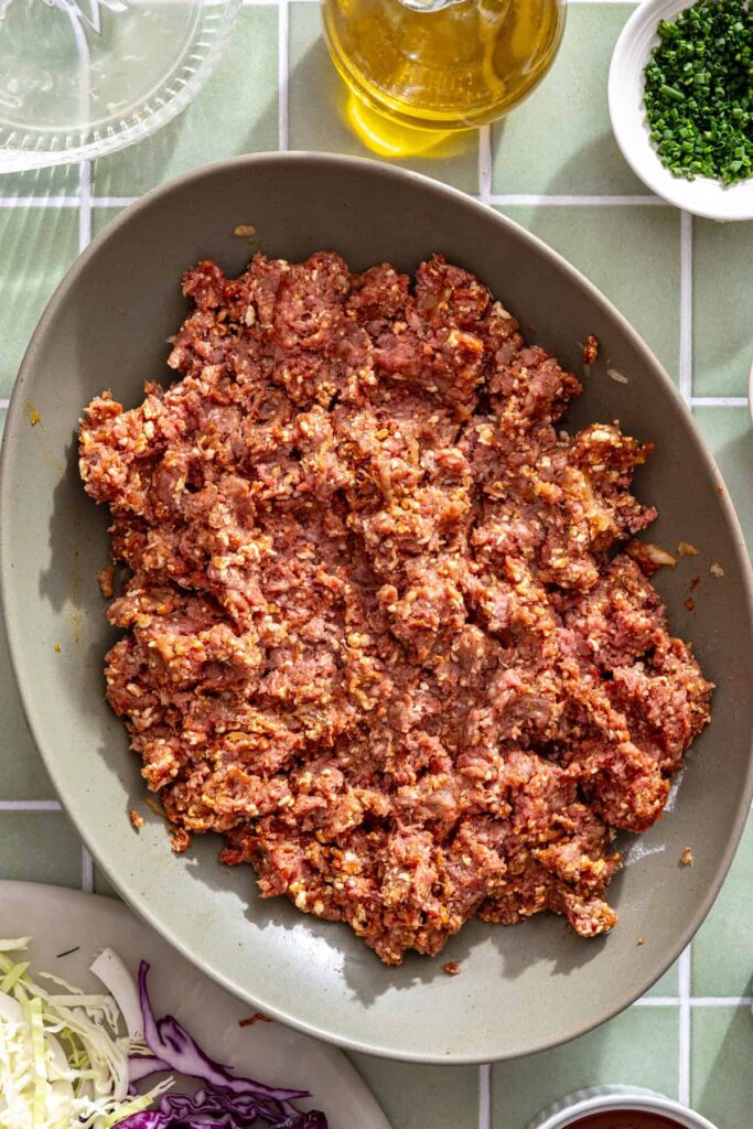 Seasoned ground beef mixture for homemade BBQ meatballs in a large mixing bowl.