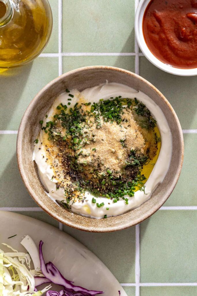 Making creamy Greek yogurt ranch with fresh dill, chives, lemon juice, and seasonings in a mixing bowl.
