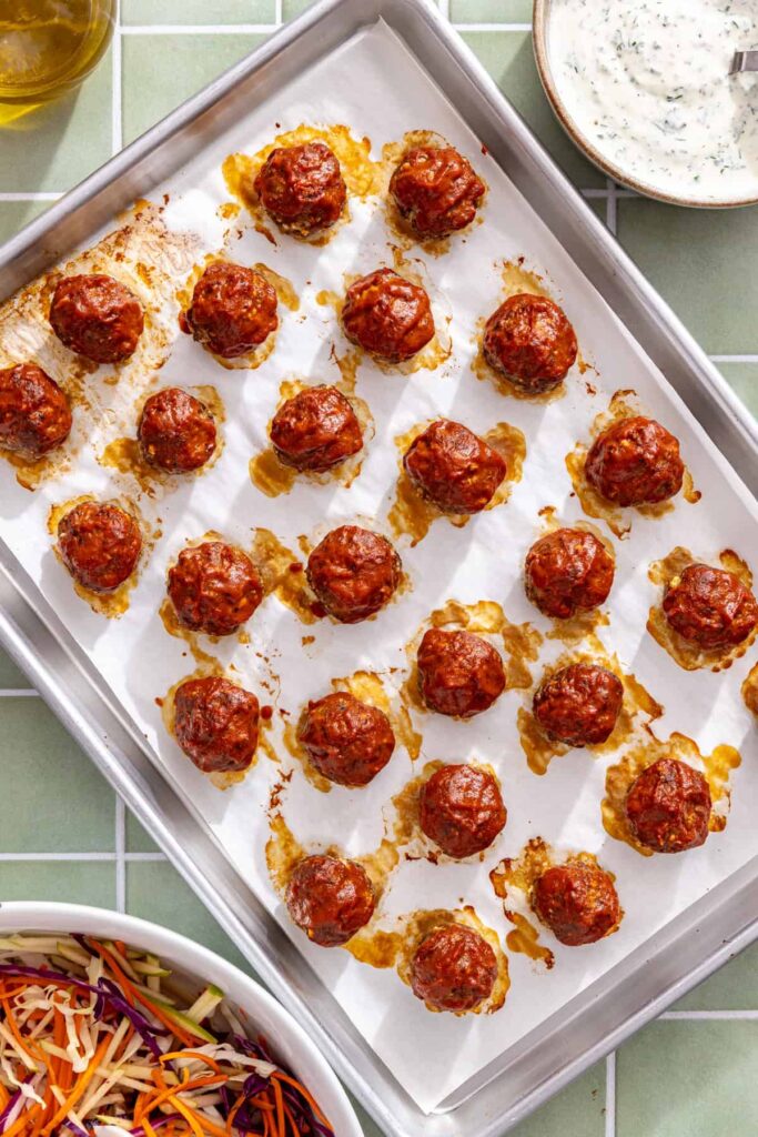 Oven-baked BBQ beef meatballs coated in a glossy barbecue glaze on a sheet pan.