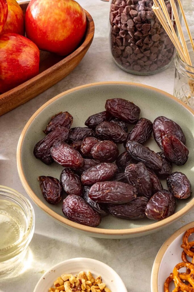 Ingredients for making a date caramel apple including an apple, dates, dark chocolate chips and coconut oil