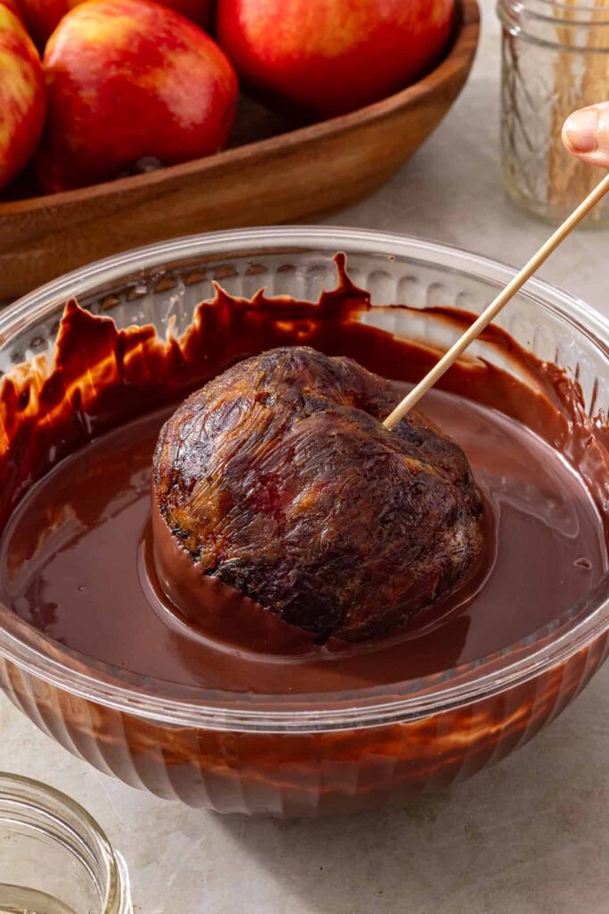 Date caramel apple being coated in melted dark chocolate