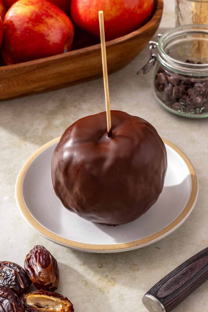 Finished date caramel apple coated in dark chocolate on a plate
