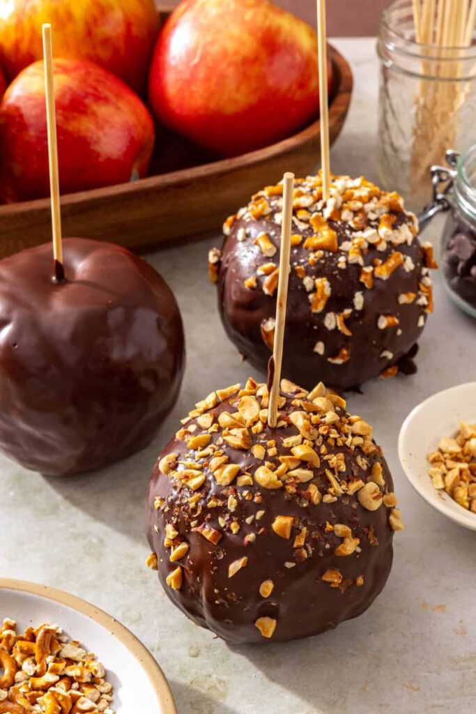 Three chocolate-covered date caramel apples topped with nuts and crushed pretzels