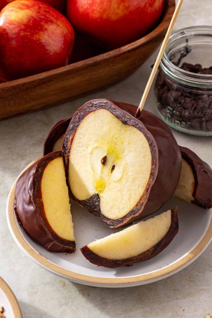 Sliced chocolate-covered date caramel apple on a plate showing the date caramel layer and apple inside