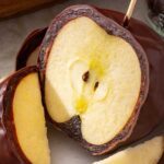 Chocolate-covered date caramel apple sliced on a plate showing the soft date caramel layer and crisp apple inside