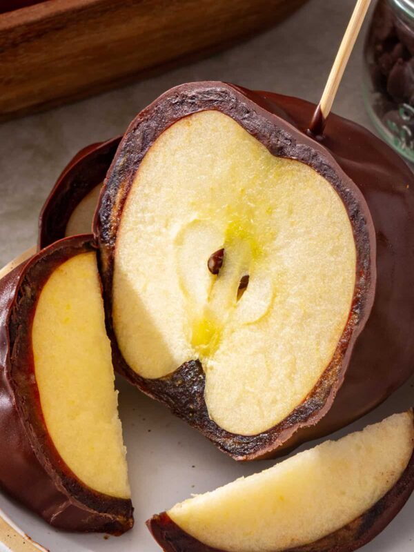 Chocolate-covered date caramel apple sliced on a plate showing the soft date caramel layer and crisp apple inside