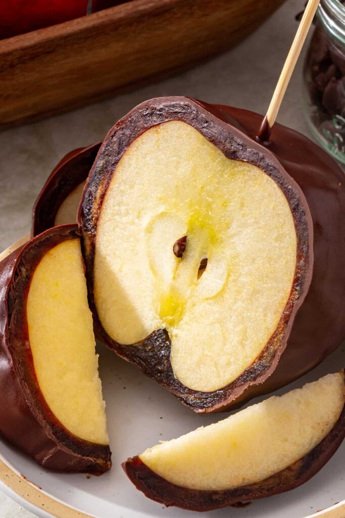 Chocolate-covered date caramel apple sliced on a plate showing the soft date caramel layer and crisp apple inside