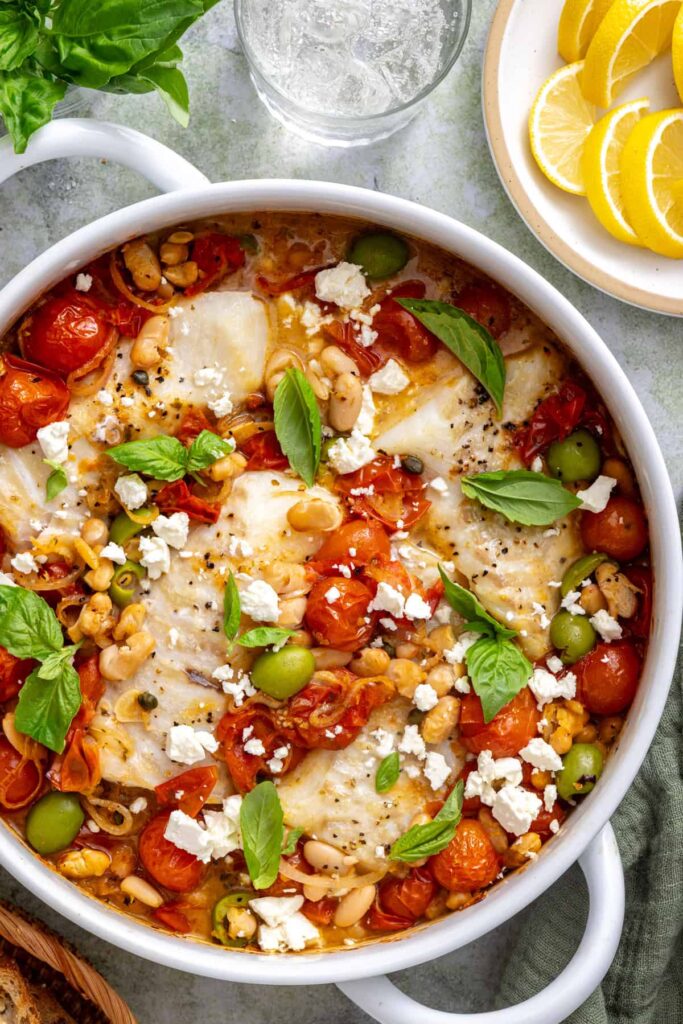 Cherry tomatoes, white beans, and flaky cod topped with crumbled feta and fresh basil in a finished skillet.