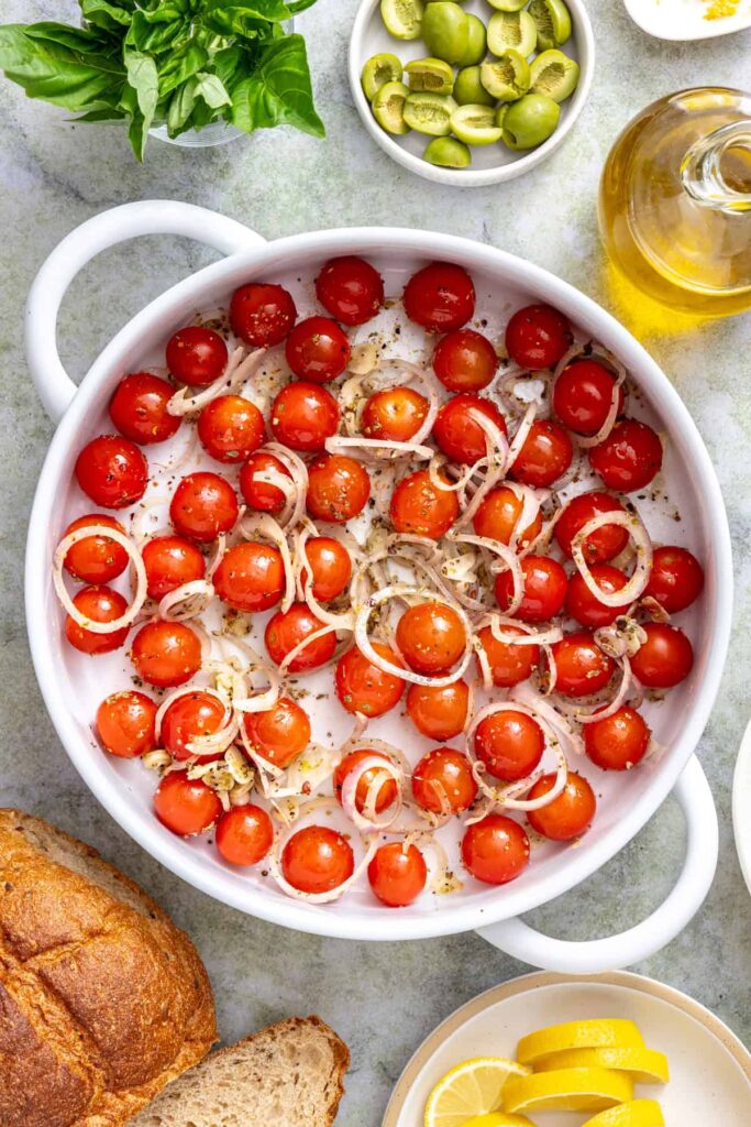 Overhead view of cherry tomatoes tossed with olive oil, garlic, shallot, and seasonings for Mediterranean baked cod.