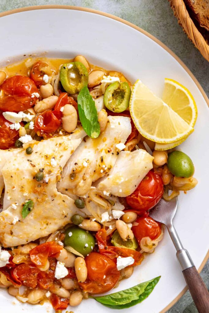 Mediterranean baked cod with tomatoes, white beans, and feta served warm with lemon wedges and toasted sourdough.
