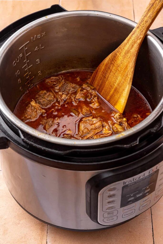 Stirring the shredded beef taco filling with lime juice and seasoning in the Instant Pot.