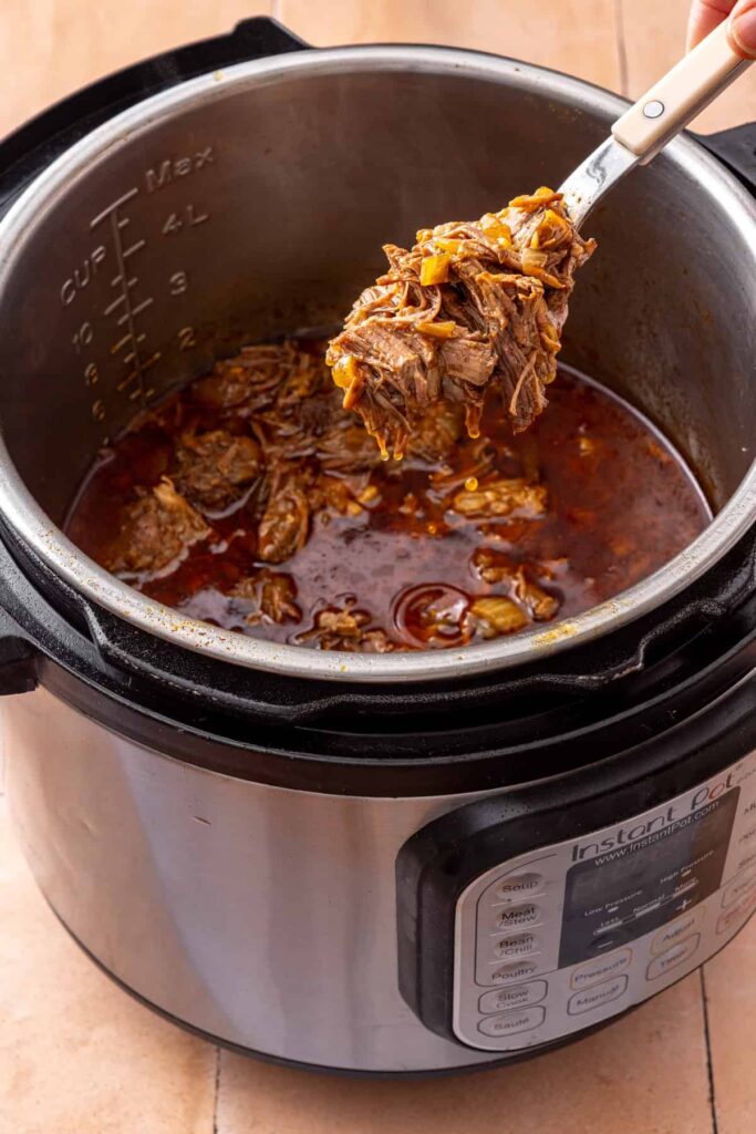 fork lifting up the finished instant pot shredded beef chuck roast, ready for sweet potato tacos