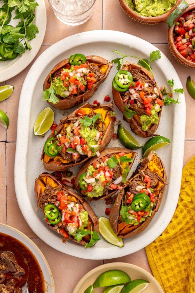Overhead view of Instant Pot beef taco stuffed sweet potatoes topped with avocado, pico de gallo, cilantro, and jalapeรฑo on a serving platter.