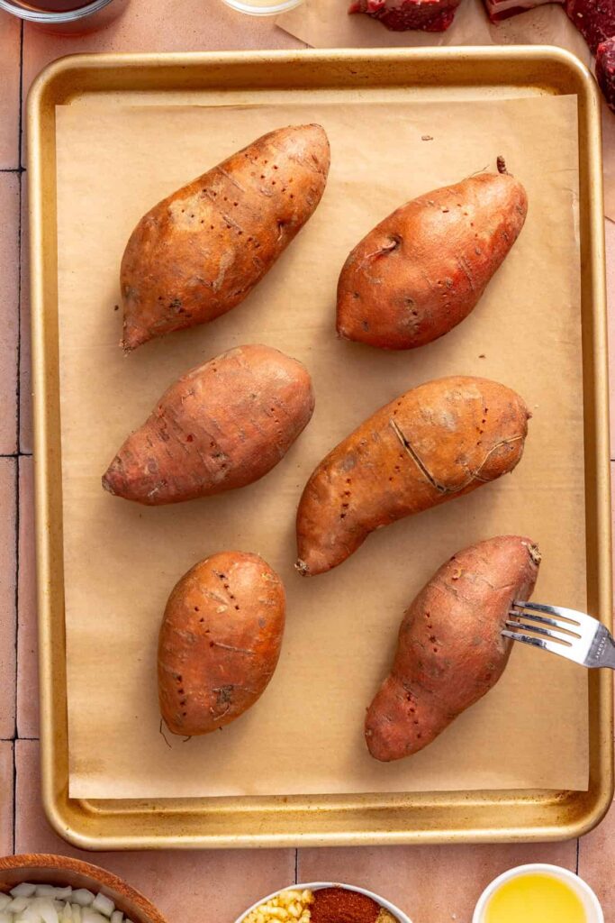 Whole sweet potatoes being pierced with a fork before baking for beef taco stuffed sweet potatoes.