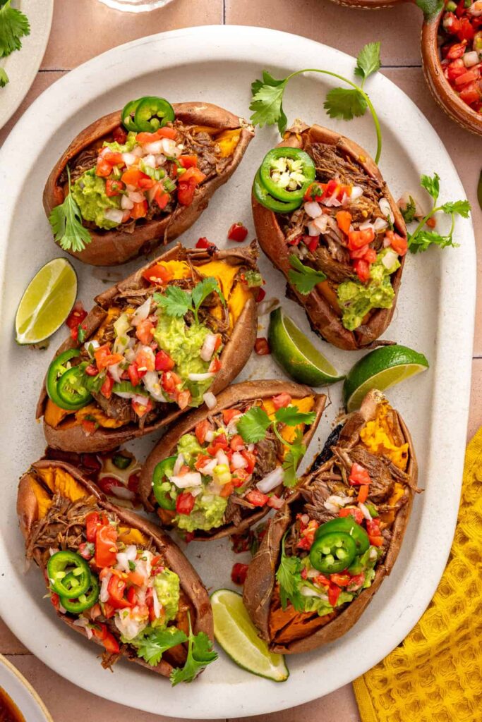 Instant Pot shredded beef stuffed sweet potatoes topped with fresh pico de gallo, avocado, and cilantro on a styled table.