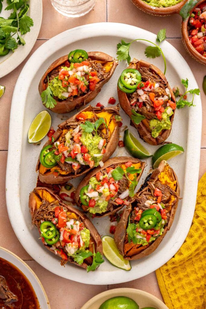 Overhead close-up of baked sweet potatoes filled with seasoned shredded beef and finished with pico de gallo, cilantro, and lime.
