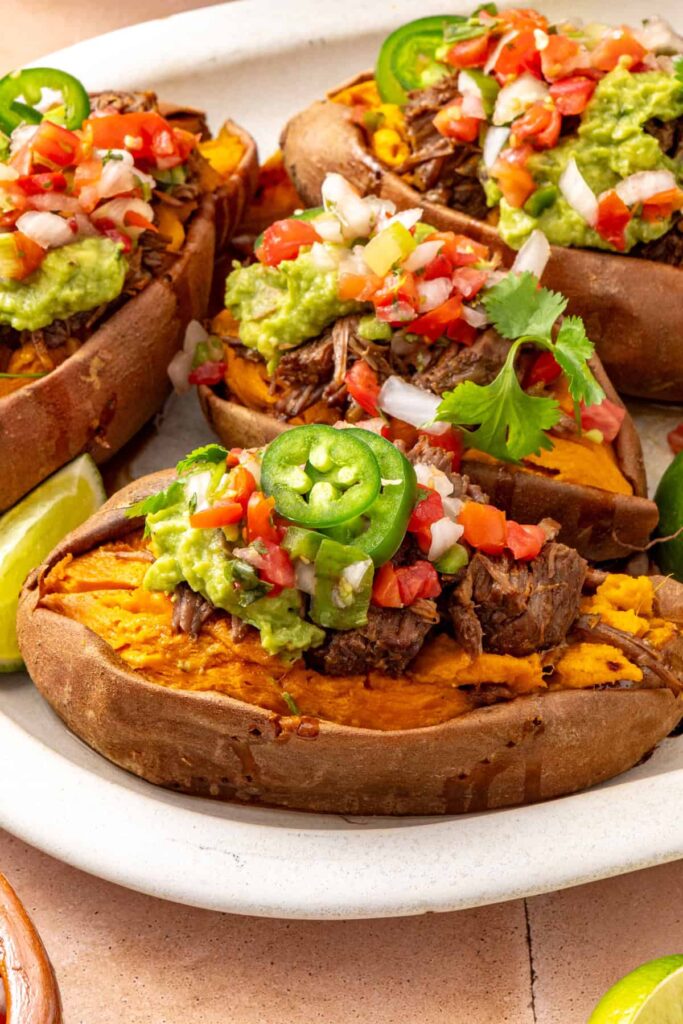 Instant Pot beef taco sweet potatoes served on a platter with fresh garnishes and the pressure cooker visible in the background.