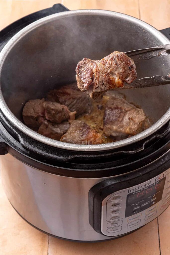 Beef chunks browning in batches in the Instant Pot for shredded beef taco sweet potatoes.