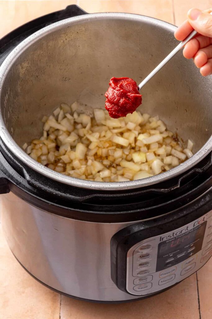 Adding tomato paste to cook with the sautéed onions in the Instant Pot.