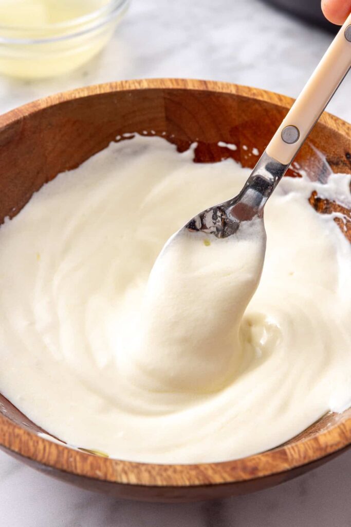 Homemade lemon garlic yogurt sauce stirred together in a small bowl to serve over Greek lemon chicken and rice.