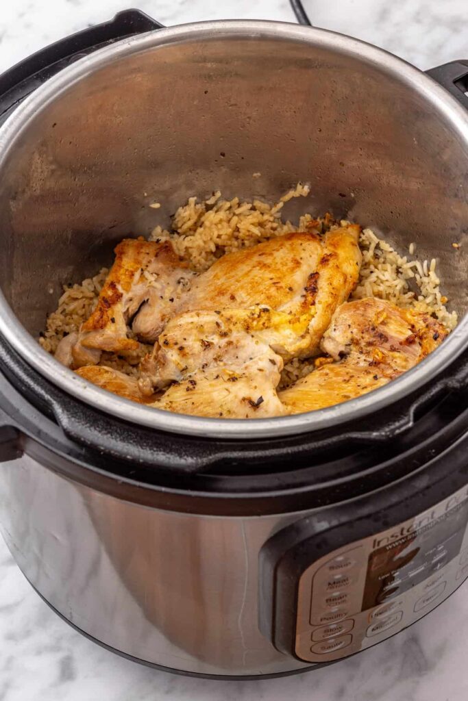 Instant Pot chicken and rice prepared for pressure cooking, with chicken thighs resting above the uncooked rice.
