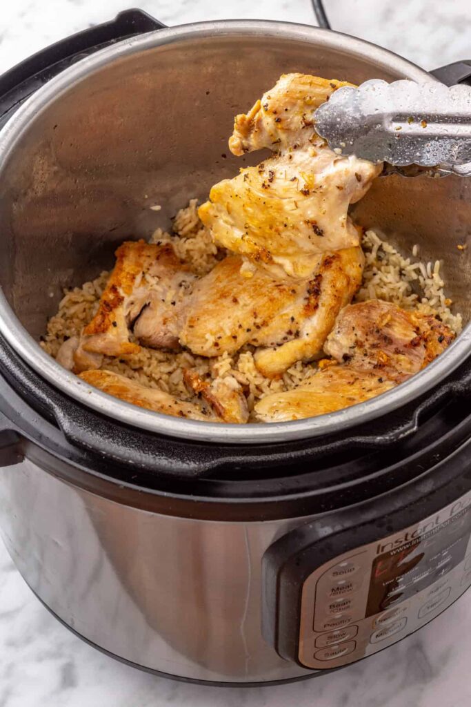 Cooked chicken thighs resting on tender lemon rice inside the Instant Pot after pressure cooking.