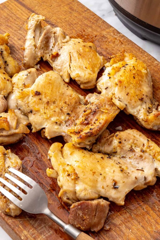 Cooked chicken thighs resting on a cutting board while the lemon rice is finished in the Instant Pot.