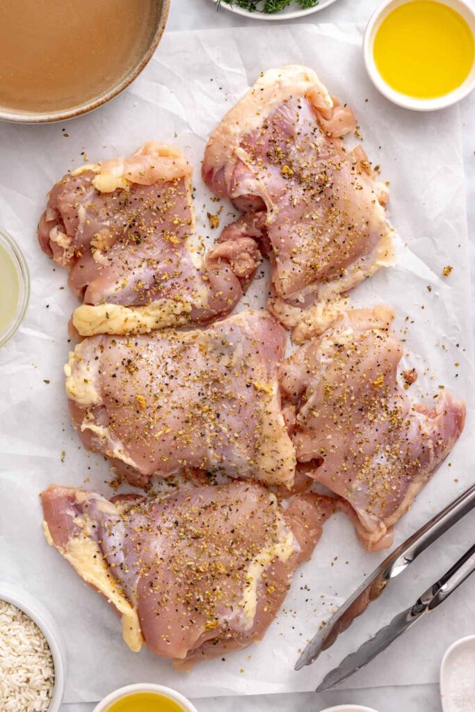 Seasoning boneless chicken thighs with oregano, garlic powder, salt, and black pepper for Greek lemon chicken.